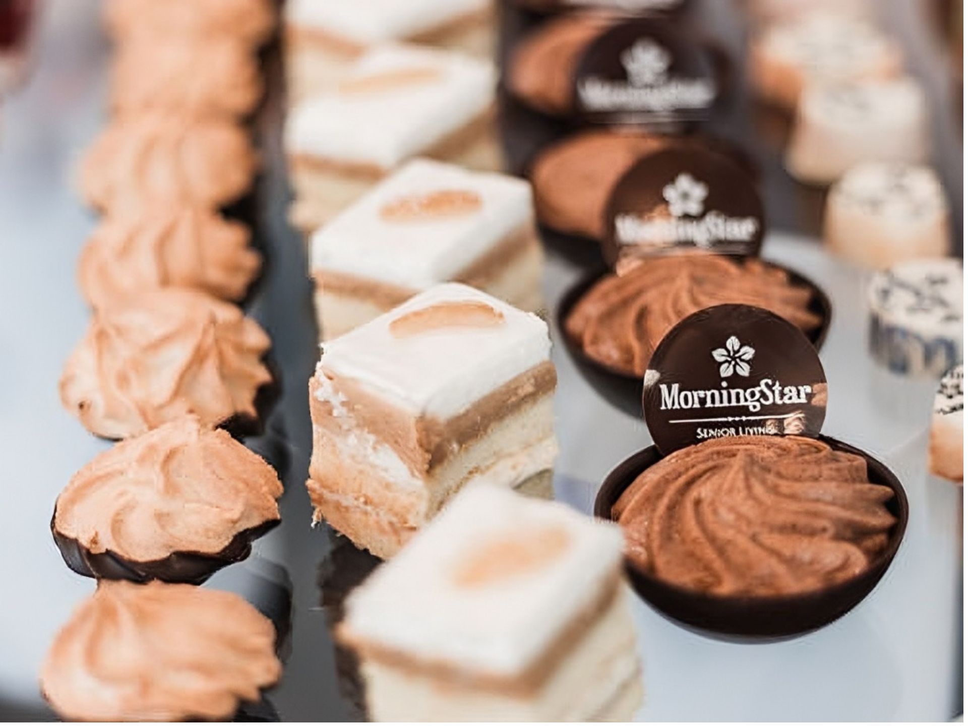 An assortment of desserts arranged on a tray, including layered cakes, meringues, and chocolate mousse cups labeled “Morningstar,” perfectly aligned in rows for residents at MorningStar Senior Living Kirkland’s vibrant retirement living community.