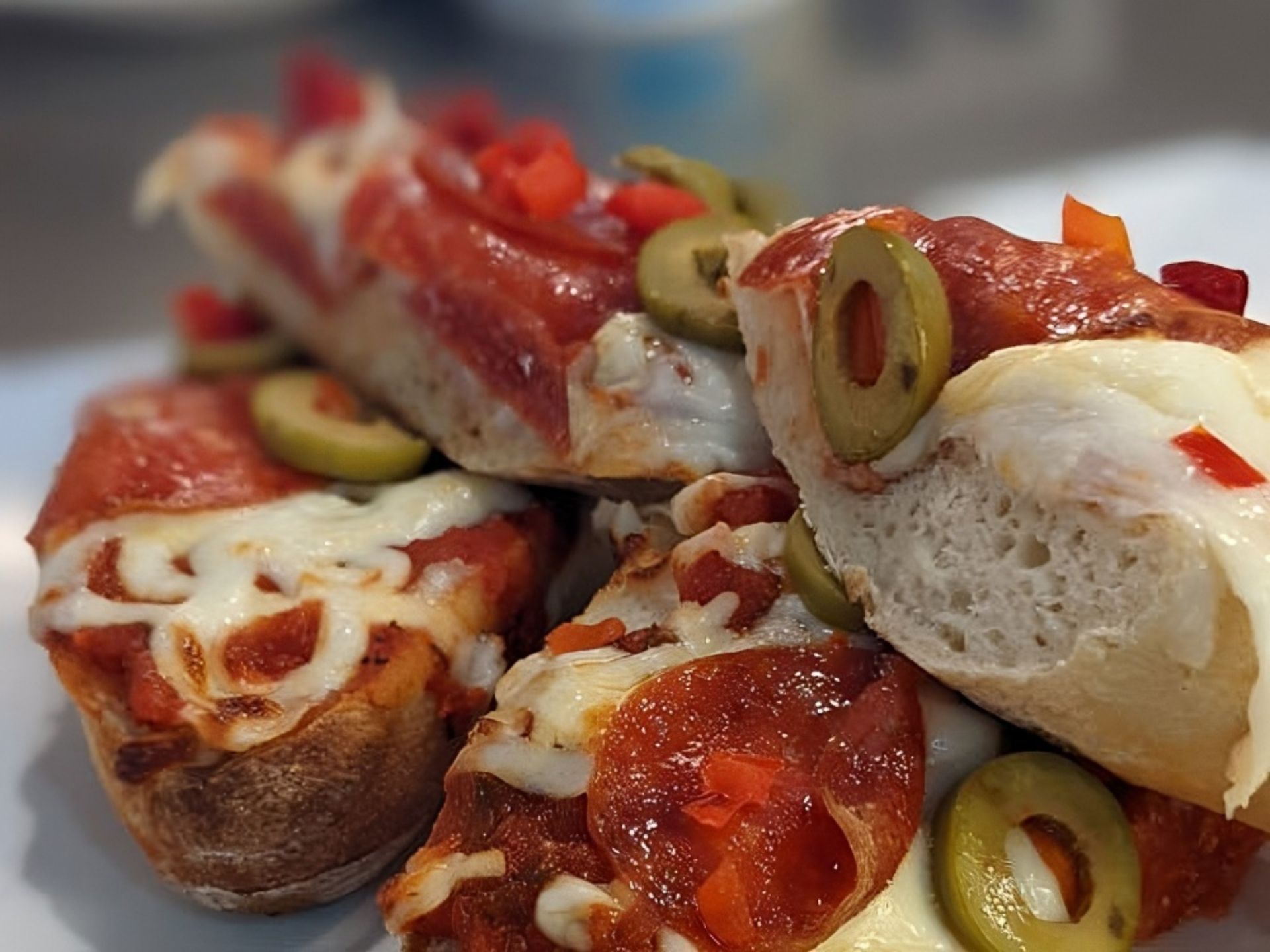 Close-up of slices of French bread pizza topped with melted mozzarella cheese, pepperoni, green olives, and chopped red peppers on a white plate at MorningStar Senior Living Kirkland's Retirement Living dining room.