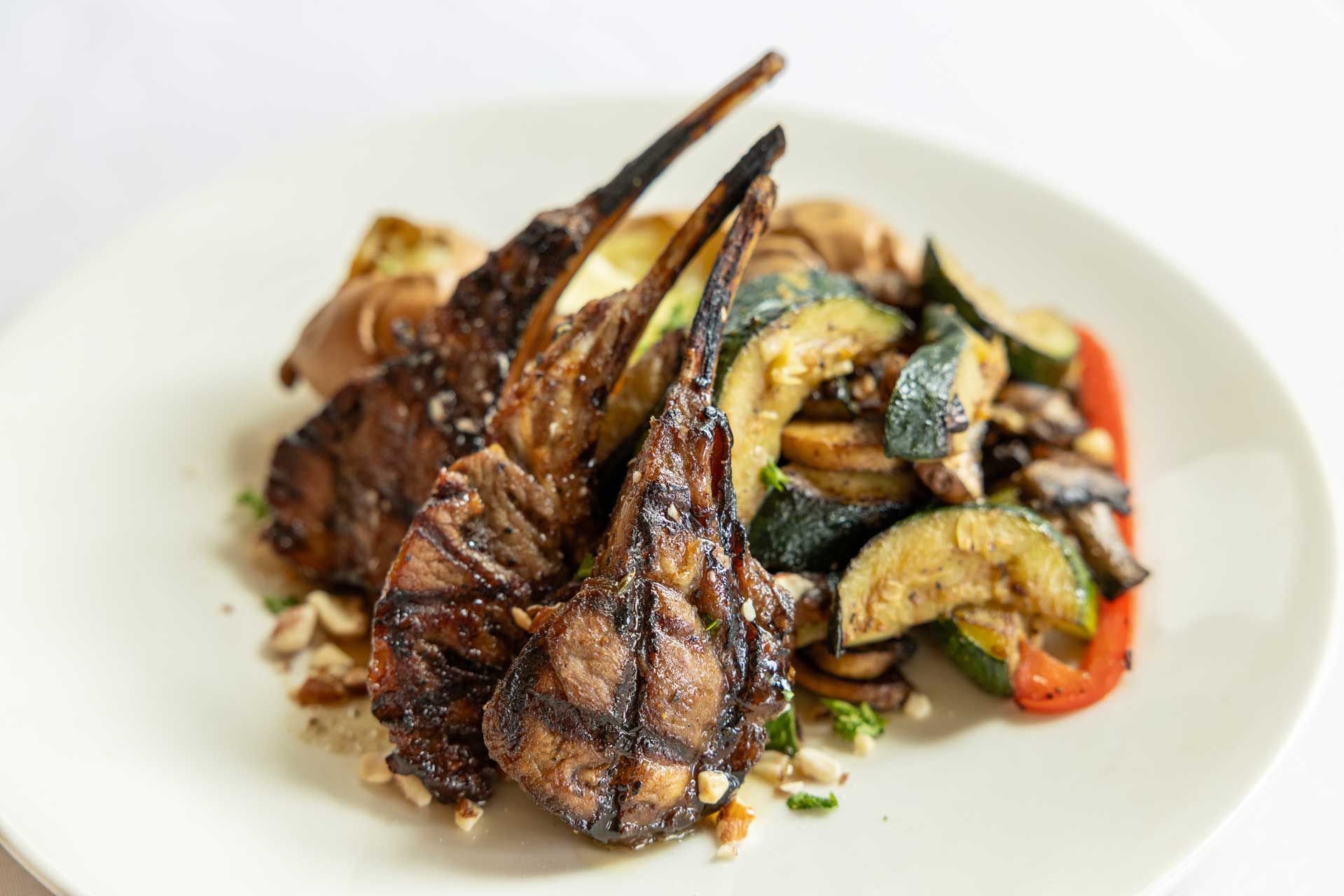 Grilled lamb chops served on a white plate with a side of sautéed vegetables, including zucchini, mushrooms, and red bell peppers—a delightful meal enjoyed at MorningStar Senior Living Kirkland's retirement living community.